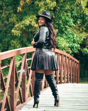 Stylish portrait on wooden bridge featuring leather jacket and thigh-high boots ensemble.