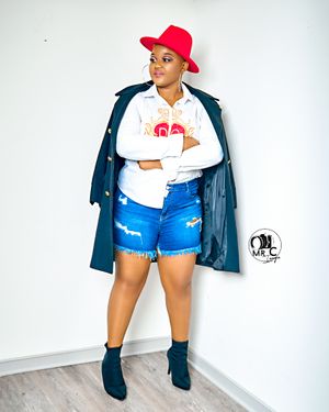 Fashionable outfit featuring denim shorts, white top, navy coat, red hat and ankle boots against white background.