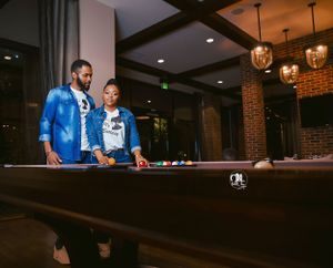 Two people playing pool in casual blue attire at dimly lit venue.