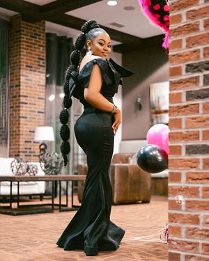 Elegant black mermaid gown portrait with balloons and brick wall background.