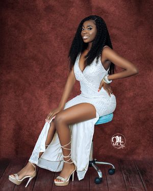 Glamour portrait on chair featuring white evening dress against burgundy background.
