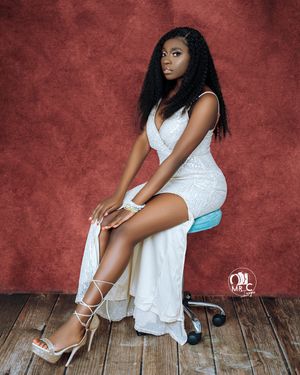 Studio portrait of a model in an elegant white dress and strappy heels against a burgundy backdrop.