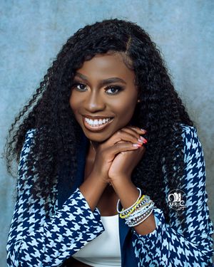 Professional headshot featuring houndstooth blazer, white top and curly hair against blue background.