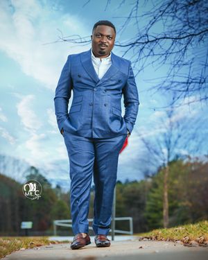 Stylish portrait of person in blue suit standing on path with autumn foliage and blue sky background.