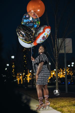 Person in geometric print dress holds colorful balloons during nighttime photo session.
