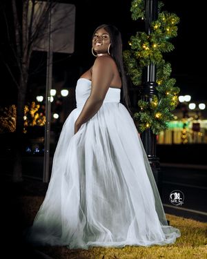 Woman in white strapless gown smiles joyfully during nighttime outdoor photo session.