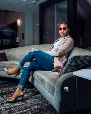 Casual yet chic portrait on grey couch wearing beige blazer and ripped jeans.