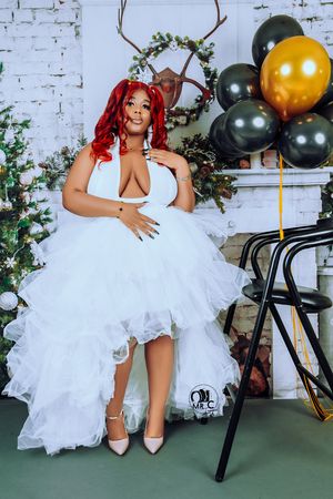 A bride in a white tulle dress and red hair poses with festive balloons and holiday decorations.