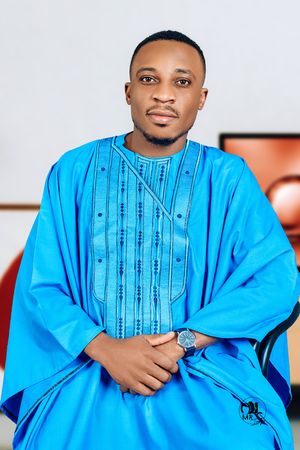 A person in a vibrant blue embroidered traditional African attire poses for a portrait.