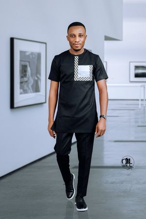 Modern casual portrait of man in black streetwear with striped accent walking in gallery.