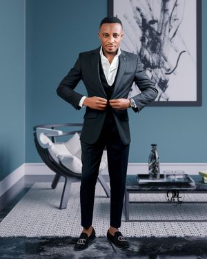 Modern fashion portrait of man in black suit adjusting jacket in contemporary interior.