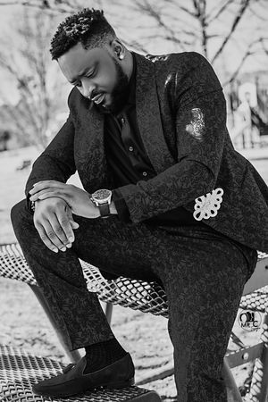 Stylish black and white portrait of a man in textured suit sitting on checkered blanket outdoors.