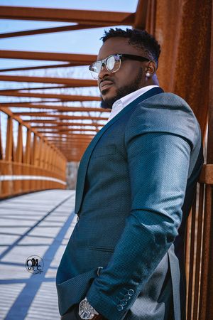 Professional fashion portrait on rustic bridge featuring blue suit and eyeglasses.