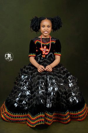 Young model wearing an elegant black and orange traditional dress with intricate beadwork against dark backdrop.