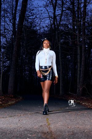 Fashionable street style portrait featuring a white turtleneck and black leather mini skirt on a forest path at dusk.