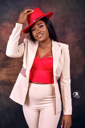 Fashion portrait with red fedora hat and blush blazer against dark background.