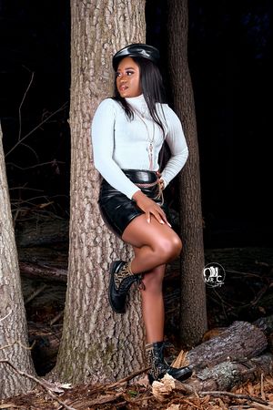 Outdoor fashion portrait against tree trunk wearing white top and leather shorts.