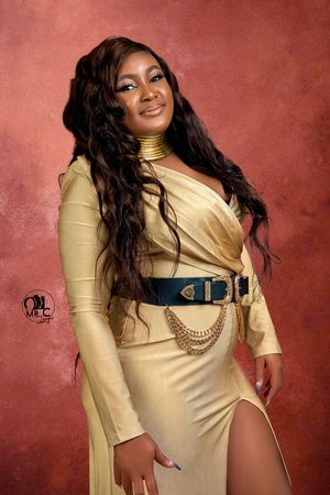 Glamorous portrait in gold dress with statement belt against dusty rose background.