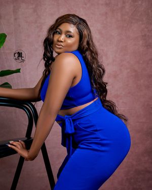Fashion portrait in royal blue two-piece outfit posed elegantly with plant decor.