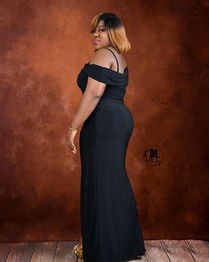 Elegant portrait of person in black off-shoulder evening gown against textured brown background.