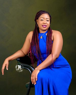 Studio portrait featuring person in blue dress with red braids seated against dark green background.