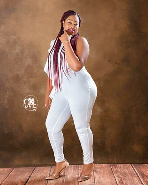Fashion portrait showing person in all-white outfit with long braids posing against brown backdrop.