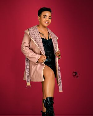 Fashion model in pink coat strikes confident pose against red studio background.