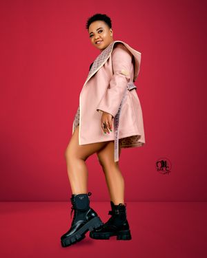 Fashion portrait of model in pink coat and black boots against vibrant red backdrop.