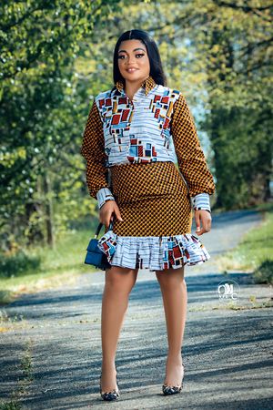 Woman in mixed print dress with geometric patterns poses on outdoor path during autumn.