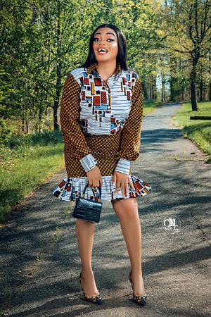 Woman in geometric print dress with brown accents poses playfully on outdoor walking path.