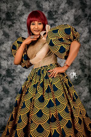 Woman in elegant gold and navy patterned ball gown with red hair poses against grey backdrop.