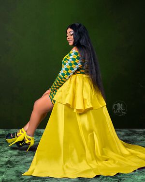 Woman in dramatic yellow gown with geometric print top poses against dark green background.