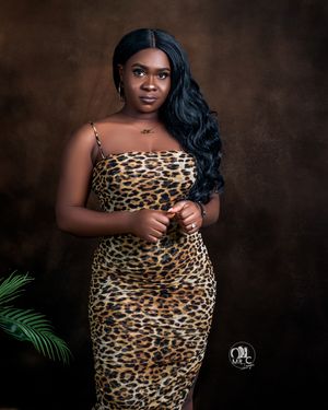 Studio portrait wearing leopard print dress with long wavy hair against brown backdrop.