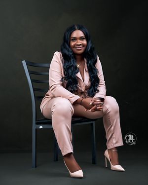 Studio portrait in salmon-colored business suit sitting casually on black chair.