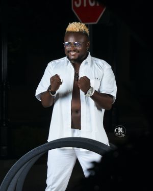 A figure in an all-white outfit poses confidently against a dark backdrop with a stop sign visible.