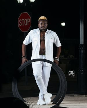 A stylish figure in white attire poses with a large black tire outdoors at night.