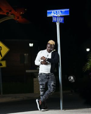 Nighttime street portrait under illuminated sign wearing distressed jeans and white top.