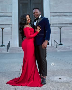 Romantic outdoor portrait featuring couple in formal red gown and navy suit against stone building.