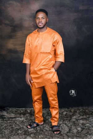 Professional portrait showing person in vibrant orange traditional African-style outfit against dark backdrop.