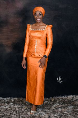 Elegant portrait featuring orange traditional African dress with matching headwrap against dark background.