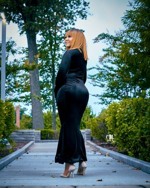 Artistic silhouette in black evening gown on outdoor walkway during golden hour.