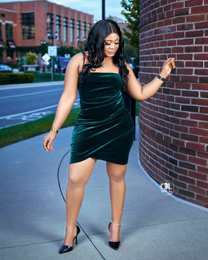 Glamorous urban photo in emerald velvet dress posed against brick wall.