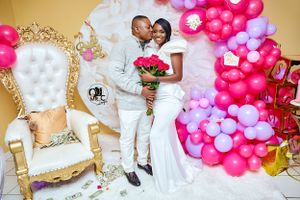Romantic wedding photo with pink and white balloon arch decorations and ornate gold throne.