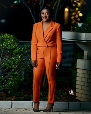 Person in vibrant orange business suit smiling against evening garden setting.