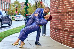 Stylish couple in matching navy blue outfits posing romantically against brick wall.