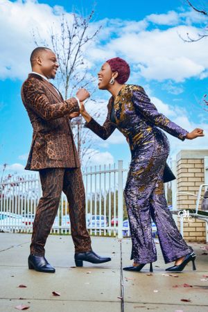 Two people in coordinating metallic suits posing playfully on sidewalk under blue sky.