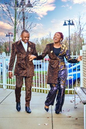 Couple wearing matching brown patterned suits laughing together outdoors on sidewalk.
