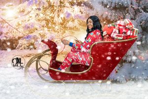 Festive holiday photo of someone in red pajamas posed in decorative Christmas sleigh.
