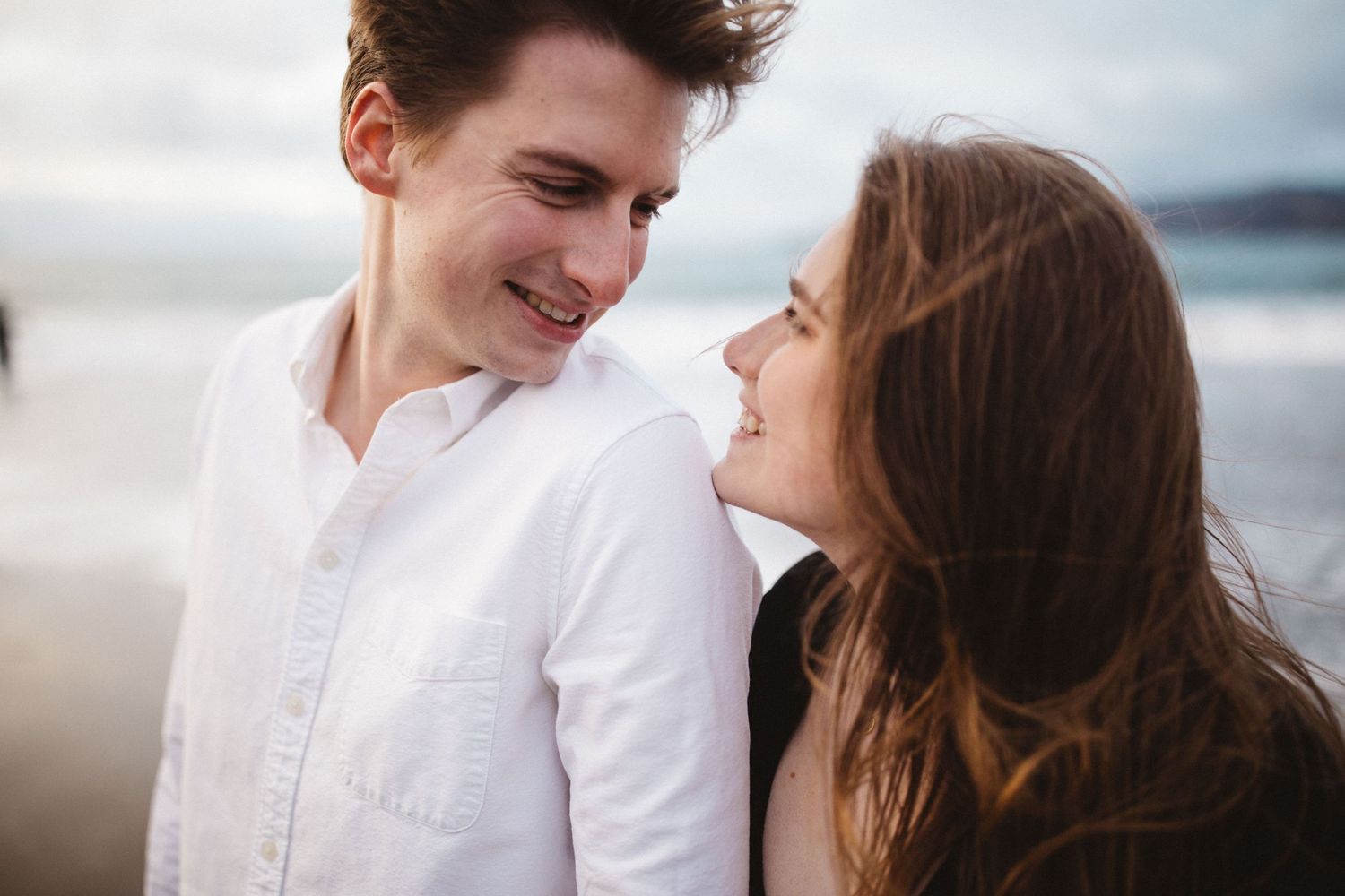 Intimate moment captured between couple on cloudy day.