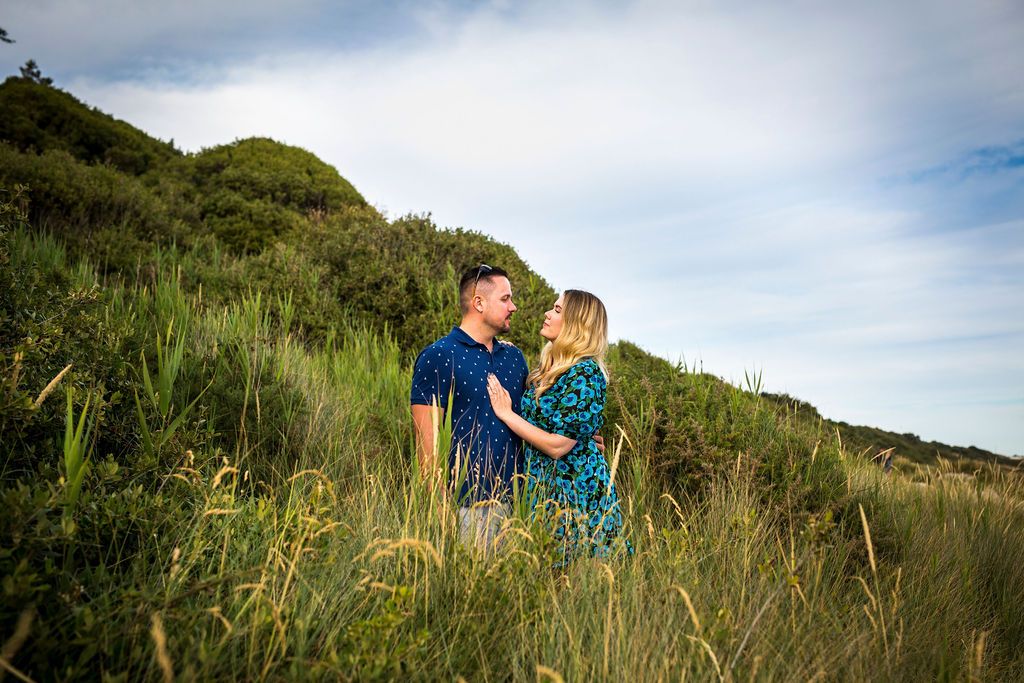 A couple shares an intimate moment on a grassy hillside overlooking the ocean.